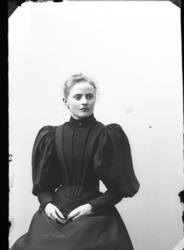 Porträtt av Ester Grönberg. Hon sitter på en stol i en mörk 