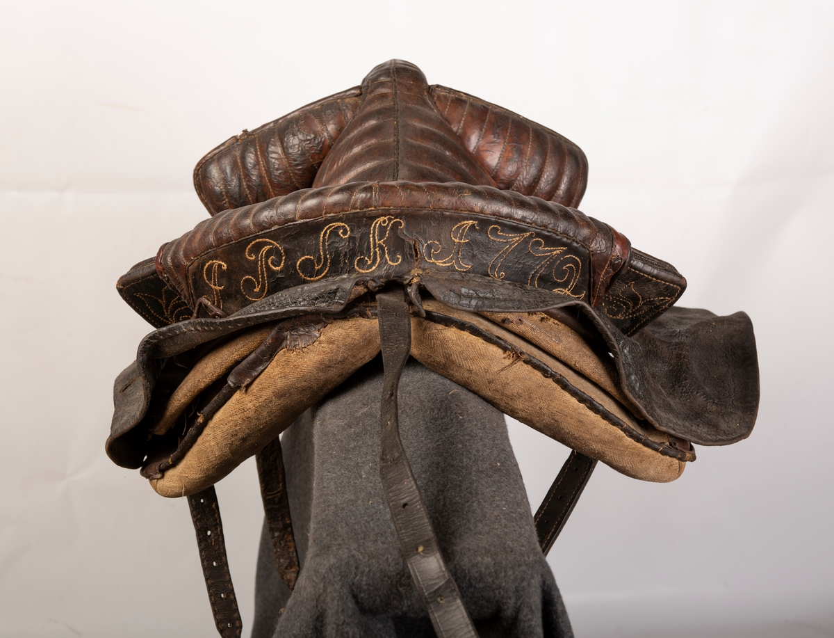 Heltrukket med lær. Initialene, antatt, JPSK og årstallet 1772 brodert på læret. 2 stigbøyler av jern, 3 lærremmer, halerem og 1 gjord. 