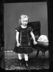 Porträtt av en liten flicka i mörk nedtill plisserad klännin