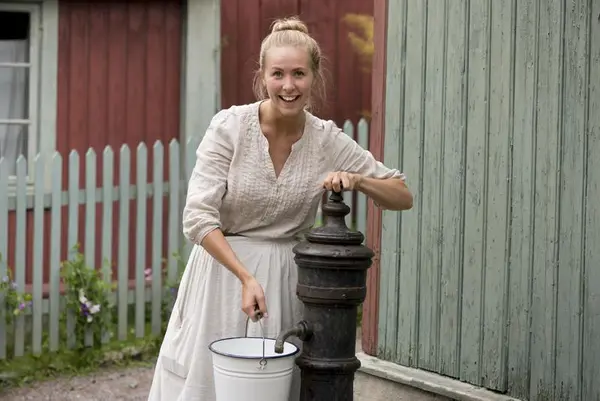 Husmor på Enerhaugen på Norsk Folkemuseum henter vann ved vannposten.