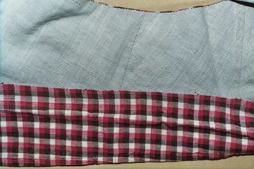 Vest i rutet bomullslerret i fargene rødt, olivengrønt/grønnnbrunt og ubleiket hvitt. Fôr og rygg i linlerret. Vesten er dobbeltspent med svarte, stofftrukne knapper. Den har sjalskrage og spensel i ryggen. Plagget er helt håndsydd. På forstykkene er det to lett skråstilte lommer og vesten buer ned midt foran.