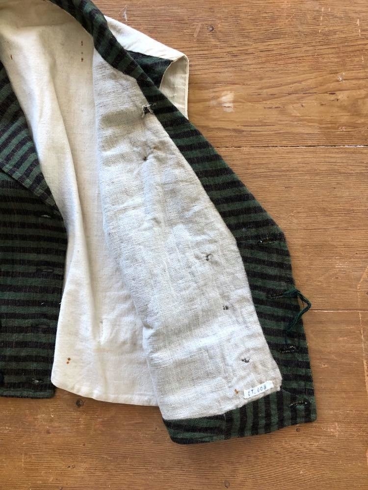 Dobbeltspent vest i ullverken, stripet i grønt og svart (sauesvart) med brun renning. Dobbel rygg i bomullslerret. Halvlinslerret (bomull/stry) i fôret i framstykkene. Vesten har fire knapphull sydd med kamgarnsullgarn og svarte knapper trukket med svart bomullssateng med brun renning. Plagget har nedbrettet krage og slag/reverser som kan kneppes mot bolen. Knapp og knapphull. Vesten buer ned midt framme og har svakt skråstilte lommer. Vattering av stry i framstykkene. I ryggen buer vesten opp midt bak. Den er vrangsydd langs ytterkantene og stukket ned med maskin, 0,8 cm fra kanten. (Registrering ved Bunad- og folkedraktrådet/Norsk institutt for bunad og folkedrakt v/Jon Fredrik Skauge, 2005, revidert v/Bjørn Sverre Hol Haugen, 2020.)