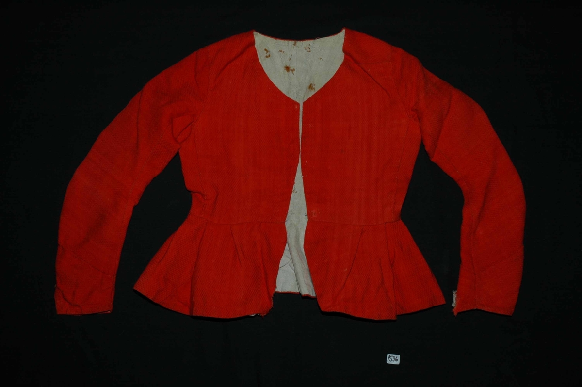 Trøye av rødt ullstoff med linfôr. Stoffet er av kamgarn og ble antageligvis solgt under betegnelsen everlasting på 1700-tallet. Produksjonssted er antageligvis England. Stoffet er i toskaft binding med flotteringer over tre tråder som gir mønstereffekt. Trøya har vært lukket med ni hekter og maljer midt framme. Snitt: Framstykkene er avdelt i midjen med kappe. Ryggstykkene går helt ned i skjøten. Kappa er foldelagt med sju folder (fra 10 cm midt framme). Foldene er 3-3,5 cm brede og 1,5 cm dype. Bua ryggsømmer sydd med spilesøm. Ryggsømmen midt bak er sydd med attersting hver for seg, men festet sammen i fôr og hovedstoff på noen steder. Det er to innsnitt under hvert herme. Ytterkantene er faldet med faldeprikkesting. Det er ekstra prikkestingsrad ved halsringing (1 cm fra ytterkant) og ved hektestillinga omlag 2 cm fra ytterkanten framme. Kappa er sydd til bolen med attersting (tre lag stoff). Fôret i bolen er bretta og lagt til og sydd ned i fôret til kappa. Kappa skrår bakover midt framme. Trange ermer sydd sammen med attersting. Sømmonnet er lagt mot bolen og fôret i bolen er lagt mot ermet og sydd til med faldesting. Skinnhemper til opphenging. Ensømserme med albuestnitt. På unerermene er det et innsnitt. Underermssømmer er sydd med attersting, stoff og fôr hver for seg (festet sammen på enkelte steder). Innsnittene er sydd med stoff og fôr sammen og lagt til en side og stukket ned, faldet til side. (Fra regsitrering ved Bunad- og folkedraktrådet/Norsk institutt for bunad og folkedrakt v/Jon Fredrik Skauge i 2005, revidert v/Bjørn Sverre Hol Haugen 2020). 