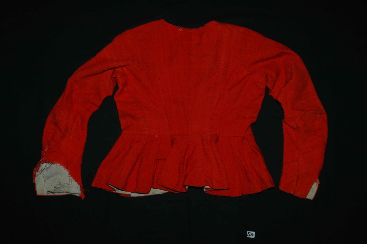 Trøye av rødt ullstoff med linfôr. Stoffet er av kamgarn og ble antageligvis solgt under betegnelsen everlasting på 1700-tallet. Produksjonssted er antageligvis England. Stoffet er i toskaft binding med flotteringer over tre tråder som gir mønstereffekt. Trøya har vært lukket med ni hekter og maljer midt framme. Snitt: Framstykkene er avdelt i midjen med kappe. Ryggstykkene går helt ned i skjøten. Kappa er foldelagt med sju folder (fra 10 cm midt framme). Foldene er 3-3,5 cm brede og 1,5 cm dype. Bua ryggsømmer sydd med spilesøm. Ryggsømmen midt bak er sydd med attersting hver for seg, men festet sammen i fôr og hovedstoff på noen steder. Det er to innsnitt under hvert herme. Ytterkantene er faldet med faldeprikkesting. Det er ekstra prikkestingsrad ved halsringing (1 cm fra ytterkant) og ved hektestillinga omlag 2 cm fra ytterkanten framme. Kappa er sydd til bolen med attersting (tre lag stoff). Fôret i bolen er bretta og lagt til og sydd ned i fôret til kappa. Kappa skrår bakover midt framme. Trange ermer sydd sammen med attersting. Sømmonnet er lagt mot bolen og fôret i bolen er lagt mot ermet og sydd til med faldesting. Skinnhemper til opphenging. Ensømserme med albuestnitt. På unerermene er det et innsnitt. Underermssømmer er sydd med attersting, stoff og fôr hver for seg (festet sammen på enkelte steder). Innsnittene er sydd med stoff og fôr sammen og lagt til en side og stukket ned, faldet til side. (Fra regsitrering ved Bunad- og folkedraktrådet/Norsk institutt for bunad og folkedrakt v/Jon Fredrik Skauge i 2005, revidert v/Bjørn Sverre Hol Haugen 2020). 