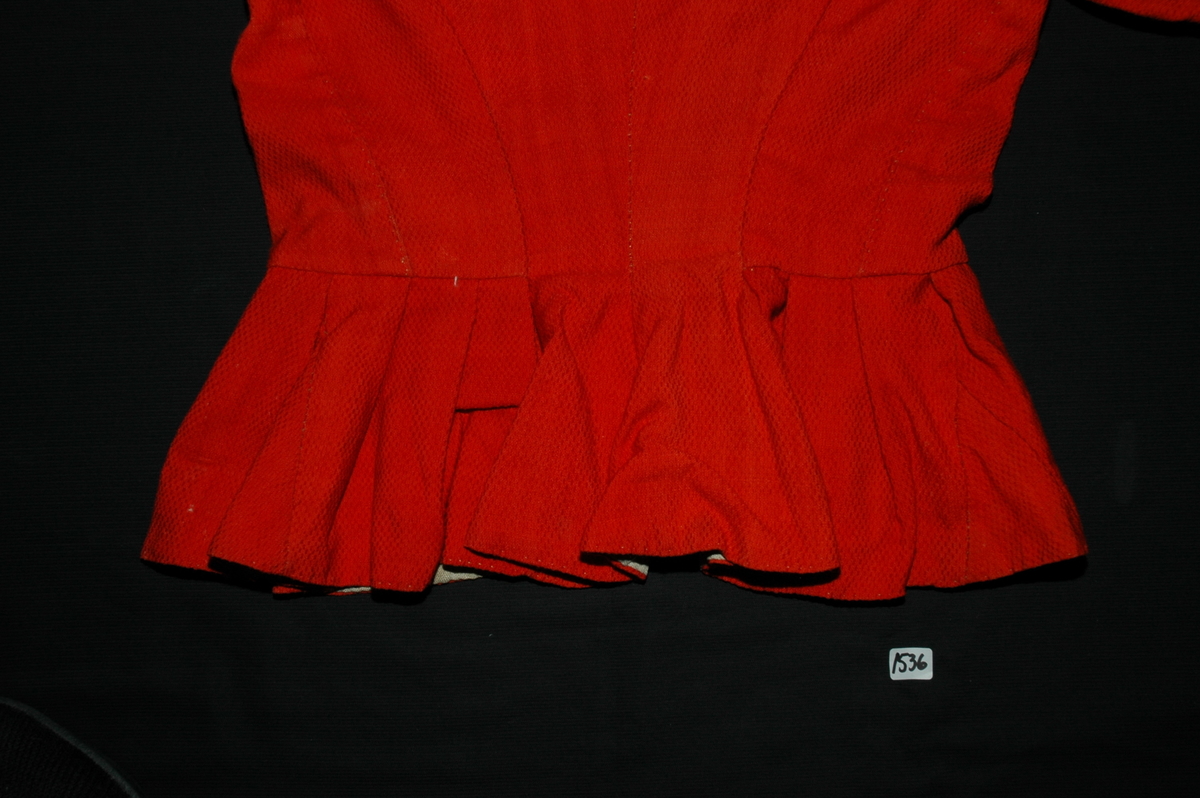 Trøye av rødt ullstoff med linfôr. Stoffet er av kamgarn og ble antageligvis solgt under betegnelsen everlasting på 1700-tallet. Produksjonssted er antageligvis England. Stoffet er i toskaft binding med flotteringer over tre tråder som gir mønstereffekt. Trøya har vært lukket med ni hekter og maljer midt framme. Snitt: Framstykkene er avdelt i midjen med kappe. Ryggstykkene går helt ned i skjøten. Kappa er foldelagt med sju folder (fra 10 cm midt framme). Foldene er 3-3,5 cm brede og 1,5 cm dype. Bua ryggsømmer sydd med spilesøm. Ryggsømmen midt bak er sydd med attersting hver for seg, men festet sammen i fôr og hovedstoff på noen steder. Det er to innsnitt under hvert herme. Ytterkantene er faldet med faldeprikkesting. Det er ekstra prikkestingsrad ved halsringing (1 cm fra ytterkant) og ved hektestillinga omlag 2 cm fra ytterkanten framme. Kappa er sydd til bolen med attersting (tre lag stoff). Fôret i bolen er bretta og lagt til og sydd ned i fôret til kappa. Kappa skrår bakover midt framme. Trange ermer sydd sammen med attersting. Sømmonnet er lagt mot bolen og fôret i bolen er lagt mot ermet og sydd til med faldesting. Skinnhemper til opphenging. Ensømserme med albuestnitt. På unerermene er det et innsnitt. Underermssømmer er sydd med attersting, stoff og fôr hver for seg (festet sammen på enkelte steder). Innsnittene er sydd med stoff og fôr sammen og lagt til en side og stukket ned, faldet til side. (Fra regsitrering ved Bunad- og folkedraktrådet/Norsk institutt for bunad og folkedrakt v/Jon Fredrik Skauge i 2005, revidert v/Bjørn Sverre Hol Haugen 2020). 