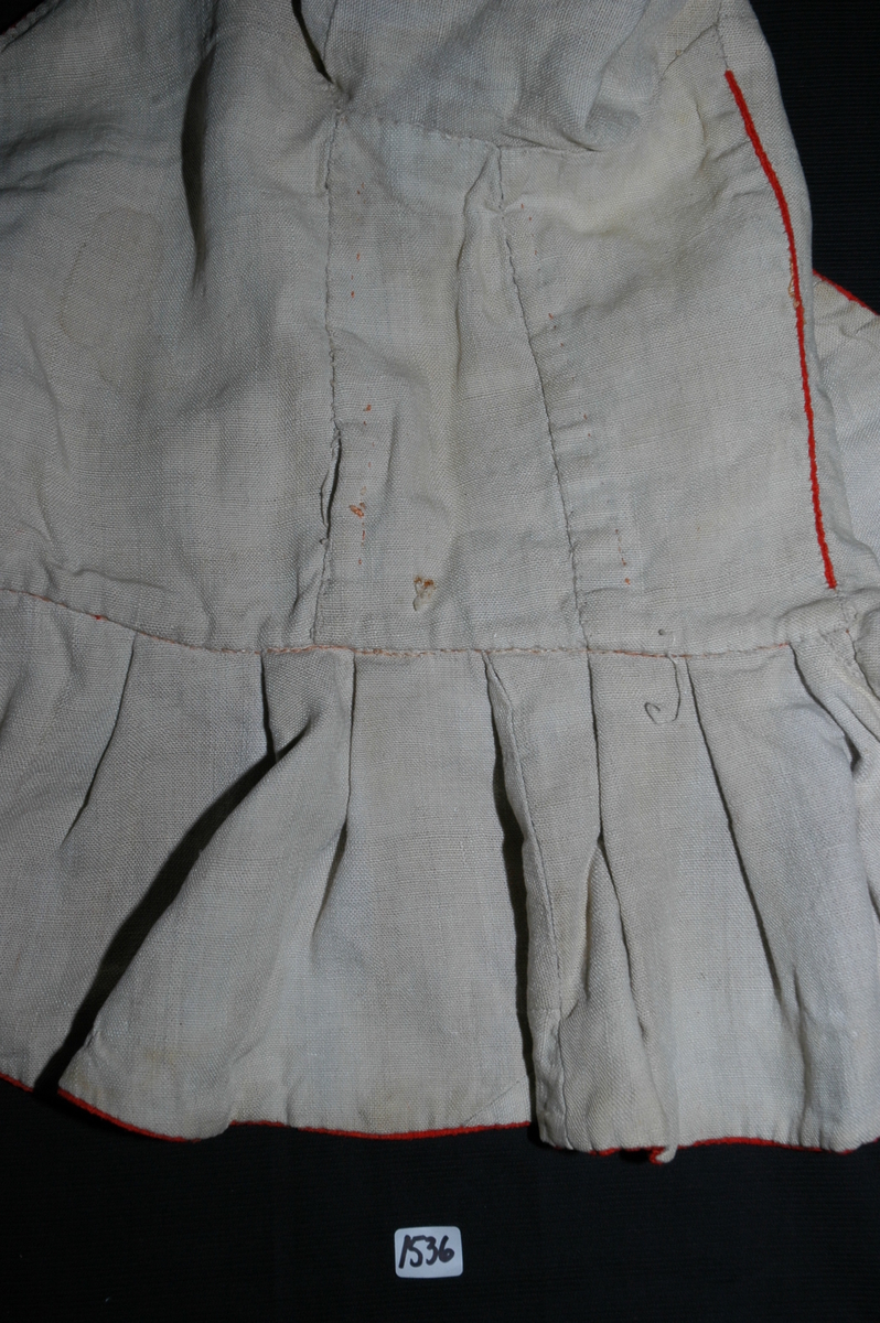 Trøye av rødt ullstoff med linfôr. Stoffet er av kamgarn og ble antageligvis solgt under betegnelsen everlasting på 1700-tallet. Produksjonssted er antageligvis England. Stoffet er i toskaft binding med flotteringer over tre tråder som gir mønstereffekt. Trøya har vært lukket med ni hekter og maljer midt framme. Snitt: Framstykkene er avdelt i midjen med kappe. Ryggstykkene går helt ned i skjøten. Kappa er foldelagt med sju folder (fra 10 cm midt framme). Foldene er 3-3,5 cm brede og 1,5 cm dype. Bua ryggsømmer sydd med spilesøm. Ryggsømmen midt bak er sydd med attersting hver for seg, men festet sammen i fôr og hovedstoff på noen steder. Det er to innsnitt under hvert herme. Ytterkantene er faldet med faldeprikkesting. Det er ekstra prikkestingsrad ved halsringing (1 cm fra ytterkant) og ved hektestillinga omlag 2 cm fra ytterkanten framme. Kappa er sydd til bolen med attersting (tre lag stoff). Fôret i bolen er bretta og lagt til og sydd ned i fôret til kappa. Kappa skrår bakover midt framme. Trange ermer sydd sammen med attersting. Sømmonnet er lagt mot bolen og fôret i bolen er lagt mot ermet og sydd til med faldesting. Skinnhemper til opphenging. Ensømserme med albuestnitt. På unerermene er det et innsnitt. Underermssømmer er sydd med attersting, stoff og fôr hver for seg (festet sammen på enkelte steder). Innsnittene er sydd med stoff og fôr sammen og lagt til en side og stukket ned, faldet til side. (Fra regsitrering ved Bunad- og folkedraktrådet/Norsk institutt for bunad og folkedrakt v/Jon Fredrik Skauge i 2005, revidert v/Bjørn Sverre Hol Haugen 2020). 