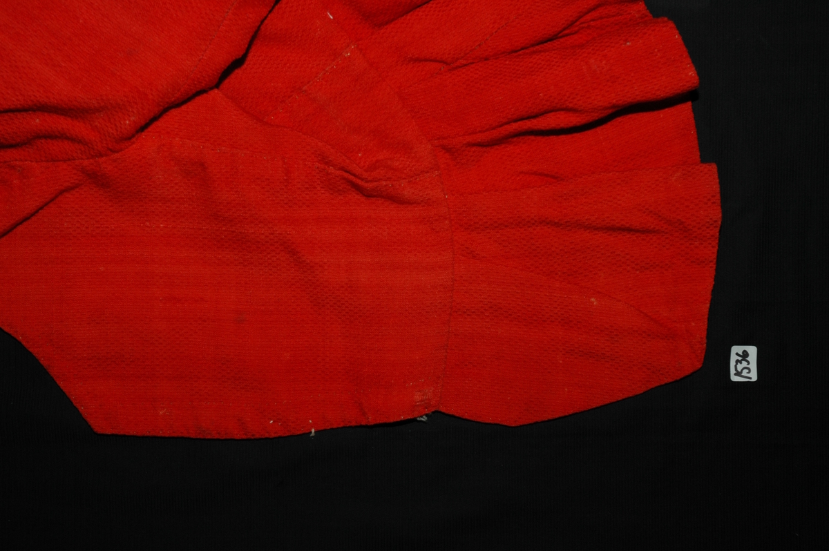 Trøye av rødt ullstoff med linfôr. Stoffet er av kamgarn og ble antageligvis solgt under betegnelsen everlasting på 1700-tallet. Produksjonssted er antageligvis England. Stoffet er i toskaft binding med flotteringer over tre tråder som gir mønstereffekt. Trøya har vært lukket med ni hekter og maljer midt framme. Snitt: Framstykkene er avdelt i midjen med kappe. Ryggstykkene går helt ned i skjøten. Kappa er foldelagt med sju folder (fra 10 cm midt framme). Foldene er 3-3,5 cm brede og 1,5 cm dype. Bua ryggsømmer sydd med spilesøm. Ryggsømmen midt bak er sydd med attersting hver for seg, men festet sammen i fôr og hovedstoff på noen steder. Det er to innsnitt under hvert herme. Ytterkantene er faldet med faldeprikkesting. Det er ekstra prikkestingsrad ved halsringing (1 cm fra ytterkant) og ved hektestillinga omlag 2 cm fra ytterkanten framme. Kappa er sydd til bolen med attersting (tre lag stoff). Fôret i bolen er bretta og lagt til og sydd ned i fôret til kappa. Kappa skrår bakover midt framme. Trange ermer sydd sammen med attersting. Sømmonnet er lagt mot bolen og fôret i bolen er lagt mot ermet og sydd til med faldesting. Skinnhemper til opphenging. Ensømserme med albuestnitt. På unerermene er det et innsnitt. Underermssømmer er sydd med attersting, stoff og fôr hver for seg (festet sammen på enkelte steder). Innsnittene er sydd med stoff og fôr sammen og lagt til en side og stukket ned, faldet til side. (Fra regsitrering ved Bunad- og folkedraktrådet/Norsk institutt for bunad og folkedrakt v/Jon Fredrik Skauge i 2005, revidert v/Bjørn Sverre Hol Haugen 2020). 