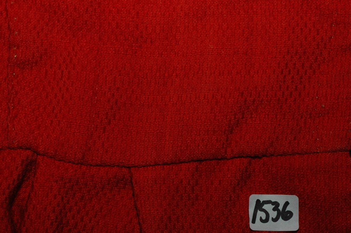 Trøye av rødt ullstoff med linfôr. Stoffet er av kamgarn og ble antageligvis solgt under betegnelsen everlasting på 1700-tallet. Produksjonssted er antageligvis England. Stoffet er i toskaft binding med flotteringer over tre tråder som gir mønstereffekt. Trøya har vært lukket med ni hekter og maljer midt framme. Snitt: Framstykkene er avdelt i midjen med kappe. Ryggstykkene går helt ned i skjøten. Kappa er foldelagt med sju folder (fra 10 cm midt framme). Foldene er 3-3,5 cm brede og 1,5 cm dype. Bua ryggsømmer sydd med spilesøm. Ryggsømmen midt bak er sydd med attersting hver for seg, men festet sammen i fôr og hovedstoff på noen steder. Det er to innsnitt under hvert herme. Ytterkantene er faldet med faldeprikkesting. Det er ekstra prikkestingsrad ved halsringing (1 cm fra ytterkant) og ved hektestillinga omlag 2 cm fra ytterkanten framme. Kappa er sydd til bolen med attersting (tre lag stoff). Fôret i bolen er bretta og lagt til og sydd ned i fôret til kappa. Kappa skrår bakover midt framme. Trange ermer sydd sammen med attersting. Sømmonnet er lagt mot bolen og fôret i bolen er lagt mot ermet og sydd til med faldesting. Skinnhemper til opphenging. Ensømserme med albuestnitt. På unerermene er det et innsnitt. Underermssømmer er sydd med attersting, stoff og fôr hver for seg (festet sammen på enkelte steder). Innsnittene er sydd med stoff og fôr sammen og lagt til en side og stukket ned, faldet til side. (Fra regsitrering ved Bunad- og folkedraktrådet/Norsk institutt for bunad og folkedrakt v/Jon Fredrik Skauge i 2005, revidert v/Bjørn Sverre Hol Haugen 2020). 