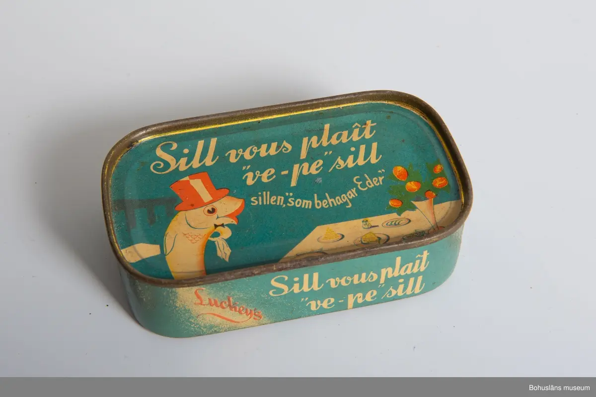 Rektangulär blå burk, vit text. På lock, botten och sidor: "Sill vous plait "ve-pe" sill, sillen, "som behagar Eder" i botten även "Innehåll
155 gram." På sidan: Luckeys, A-B. Elis Luckeys Konservfabrik Lysekil,
Sweden" och engelsk innehållsdeklaration.
Se även UM17232.
