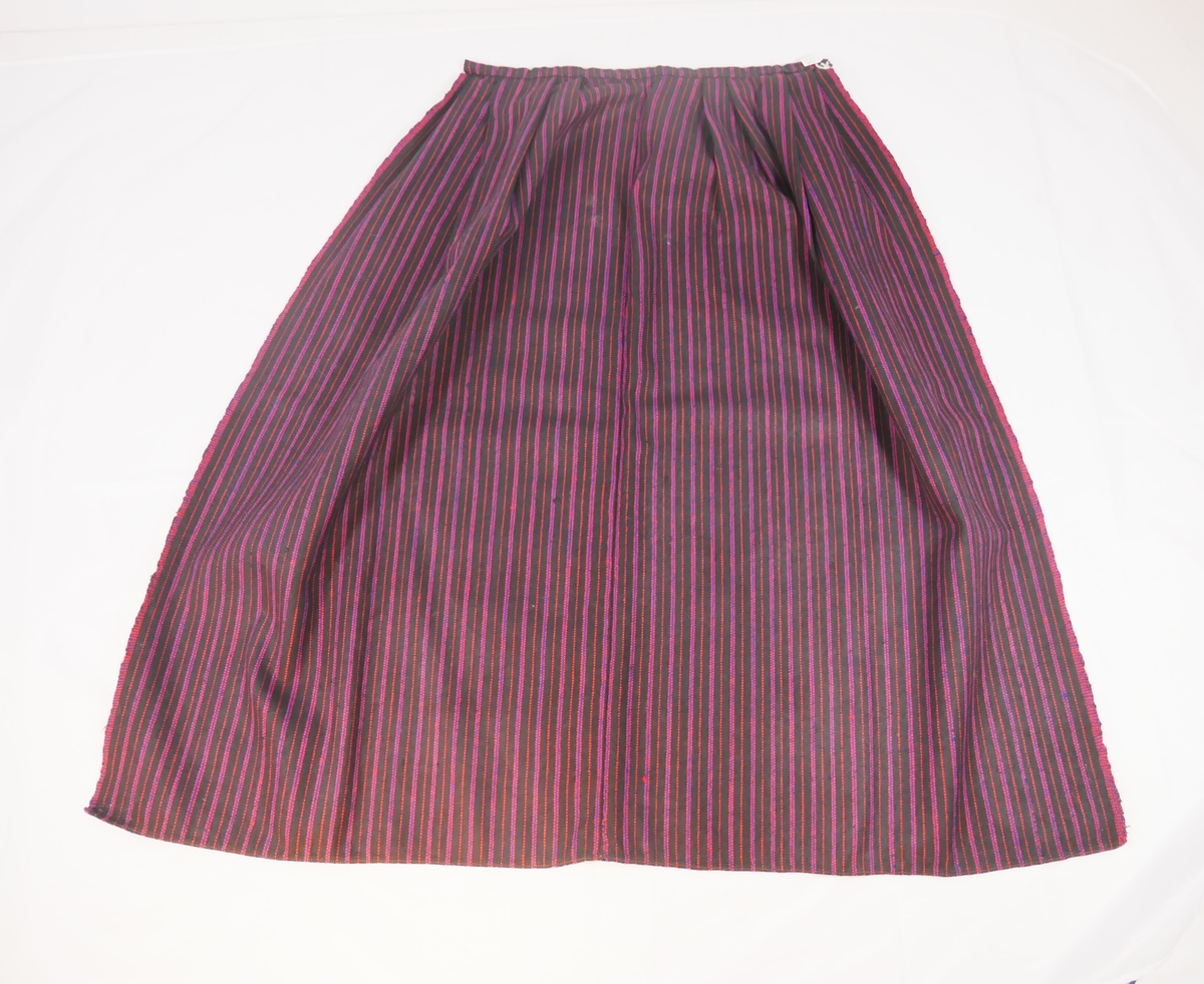 Forkle, randa. Også reg. som L.nr. 1987-102. vove i to lengder som er sydd saman midt framme med maskinsaum. Smal fald nede sydd med maskin. Linning av forklestoffet. To folder framovervende og to bakovervende på kvar side av eit glatt midtparti. Krok i kvar side av linningen