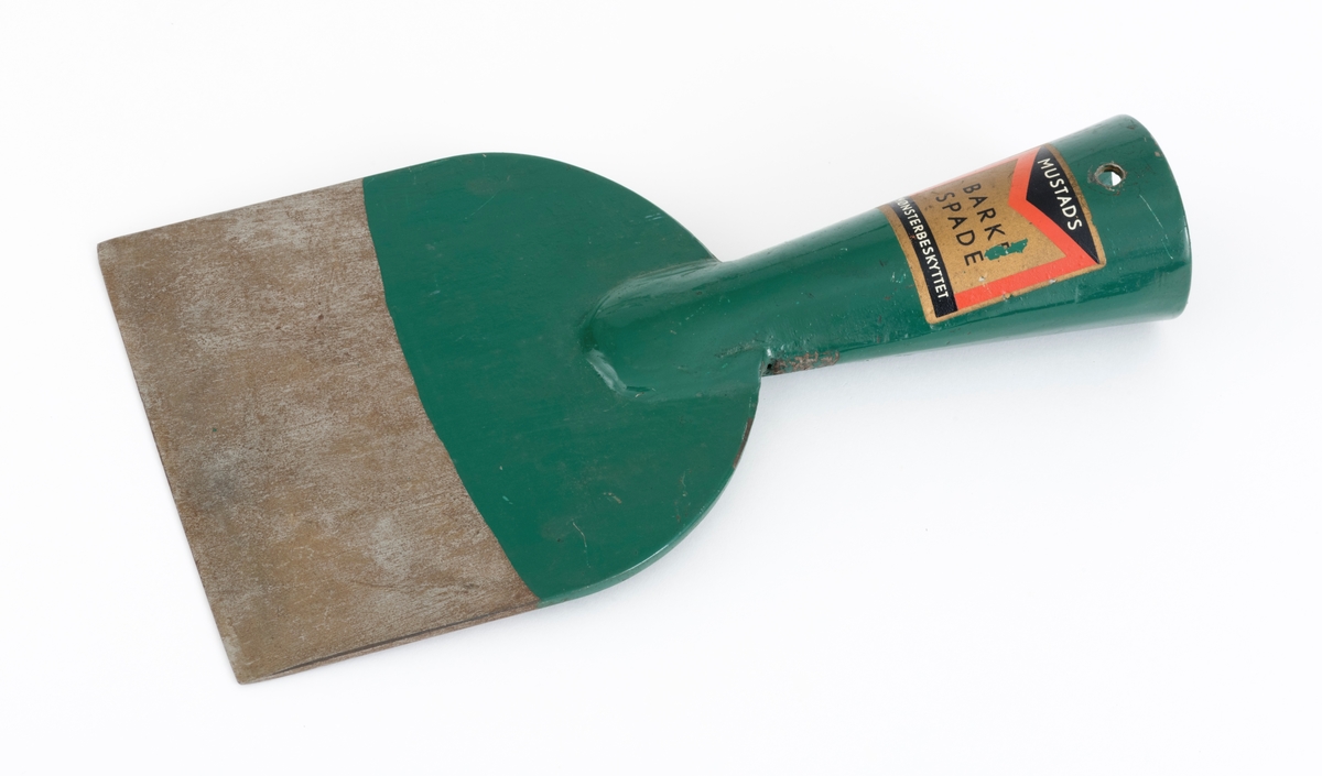 Barkespade fra O. Mustads fabrikker. Barkespaden består av ei plan stålplate med ei påsveiset, kon stålhylse i forlengelsen av bladets midtakse, i overenden.  Bladet er 12 centimeter bredt ved eggen, og egglinja er ubetydelig konvekst buet.  Den øvre enden av bladet var derimot tydelig buet, nærmest halvsirkelformet.  Her er bladet drøyt 4 millimeter tjukt.  Falen er lagd av 3 millimeter tjukt stål.  Den er tilpasset en kjegleformet skaftende og har et gjennombrutt hull med cirka 5 millimeters diameter, antakelig for en skrue eller spiker som skulle forebygge at stålet løsnet fra treskaftet.  Den øvre delen av bladet og falen er innsatt med mørkegrønn lakk.  På falens ytterside er det påsatt en rektangulær etikett med en rød «M» for Mustad på gullfarget og svart botn.  På den samme etiketten finner vi teksten «MUSTADS BARKESPADE MØNSTERBESKYTTET».  Denne barkespaden har ingen nevneverdige slitasjespor som kan tyde på at den har vært brukt i skogen, og den har sannsynligvis aldri vært skjeftet.