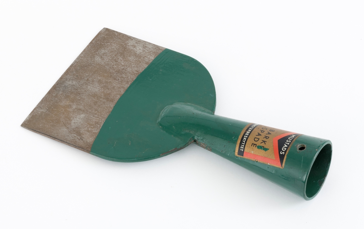 Barkespade fra O. Mustads fabrikker. Barkespaden består av ei plan stålplate med ei påsveiset, kon stålhylse i forlengelsen av bladets midtakse, i overenden.  Bladet er 12 centimeter bredt ved eggen, og egglinja er ubetydelig konvekst buet.  Den øvre enden av bladet var derimot tydelig buet, nærmest halvsirkelformet.  Her er bladet drøyt 4 millimeter tjukt.  Falen er lagd av 3 millimeter tjukt stål.  Den er tilpasset en kjegleformet skaftende og har et gjennombrutt hull med cirka 5 millimeters diameter, antakelig for en skrue eller spiker som skulle forebygge at stålet løsnet fra treskaftet.  Den øvre delen av bladet og falen er innsatt med mørkegrønn lakk.  På falens ytterside er det påsatt en rektangulær etikett med en rød «M» for Mustad på gullfarget og svart botn.  På den samme etiketten finner vi teksten «MUSTADS BARKESPADE MØNSTERBESKYTTET».  Denne barkespaden har ingen nevneverdige slitasjespor som kan tyde på at den har vært brukt i skogen, og den har sannsynligvis aldri vært skjeftet.