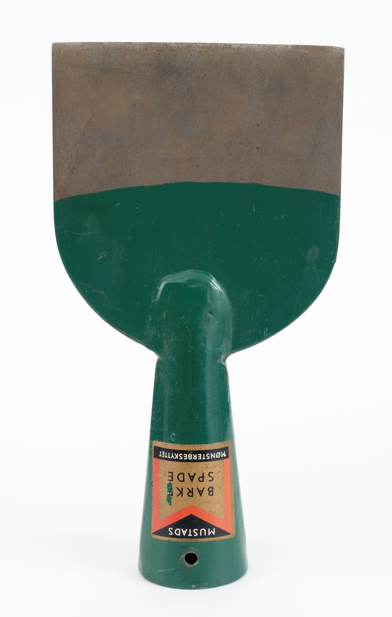 Barkespade fra O. Mustads fabrikker. Barkespaden består av ei plan stålplate med ei påsveiset, kon stålhylse i forlengelsen av bladets midtakse, i overenden.  Bladet er 12 centimeter bredt ved eggen, og egglinja er ubetydelig konvekst buet.  Den øvre enden av bladet var derimot tydelig buet, nærmest halvsirkelformet.  Her er bladet drøyt 4 millimeter tjukt.  Falen er lagd av 3 millimeter tjukt stål.  Den er tilpasset en kjegleformet skaftende og har et gjennombrutt hull med cirka 5 millimeters diameter, antakelig for en skrue eller spiker som skulle forebygge at stålet løsnet fra treskaftet.  Den øvre delen av bladet og falen er innsatt med mørkegrønn lakk.  På falens ytterside er det påsatt en rektangulær etikett med en rød «M» for Mustad på gullfarget og svart botn.  På den samme etiketten finner vi teksten «MUSTADS BARKESPADE MØNSTERBESKYTTET».  Denne barkespaden har ingen nevneverdige slitasjespor som kan tyde på at den har vært brukt i skogen, og den har sannsynligvis aldri vært skjeftet.
