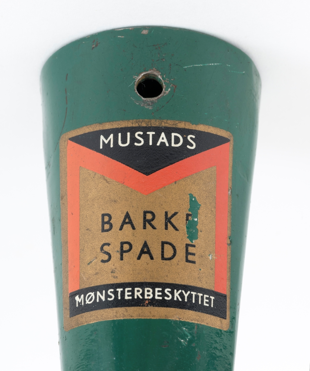 Barkespade fra O. Mustads fabrikker. Barkespaden består av ei plan stålplate med ei påsveiset, kon stålhylse i forlengelsen av bladets midtakse, i overenden.  Bladet er 12 centimeter bredt ved eggen, og egglinja er ubetydelig konvekst buet.  Den øvre enden av bladet var derimot tydelig buet, nærmest halvsirkelformet.  Her er bladet drøyt 4 millimeter tjukt.  Falen er lagd av 3 millimeter tjukt stål.  Den er tilpasset en kjegleformet skaftende og har et gjennombrutt hull med cirka 5 millimeters diameter, antakelig for en skrue eller spiker som skulle forebygge at stålet løsnet fra treskaftet.  Den øvre delen av bladet og falen er innsatt med mørkegrønn lakk.  På falens ytterside er det påsatt en rektangulær etikett med en rød «M» for Mustad på gullfarget og svart botn.  På den samme etiketten finner vi teksten «MUSTADS BARKESPADE MØNSTERBESKYTTET».  Denne barkespaden har ingen nevneverdige slitasjespor som kan tyde på at den har vært brukt i skogen, og den har sannsynligvis aldri vært skjeftet.