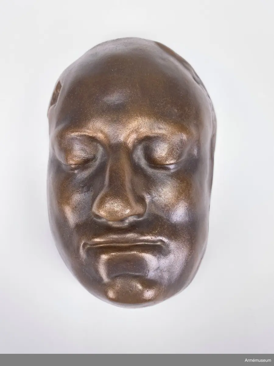 Bronsmask föreställande den döde Karl XII.

Enl styresman Olle Cederlöfs anteckningar med anledning av gåva AM.066063 (AM 73/475) är detta inte en dödsmask. 

"Proportionerna i ansiktet stämmer inte med kraniets proportioner enl 1918 års gravöppning - utan en av den schweiziske medaljgravören Hedlinger gjord frihandsmodellering inför konungens lik på Karlberg 1718. Hedlingers modell nu endast avsedd att ligga till grund för hans uppdrag: Att modellera en reliefbild för konungens mynt och minnespenningar. Hedlinger anlände till Sverige 1718-. Konungen hade då avlidit och Hedlinger hade aldrig sett Karl XII i levande livet, han tog chansen att fånga konungens ansikte inför 'lit de parade' på Karlberg. Hedlingers 'dödsmask' har senare avgjutits i gips, brons och  järn i olika sammanhang."