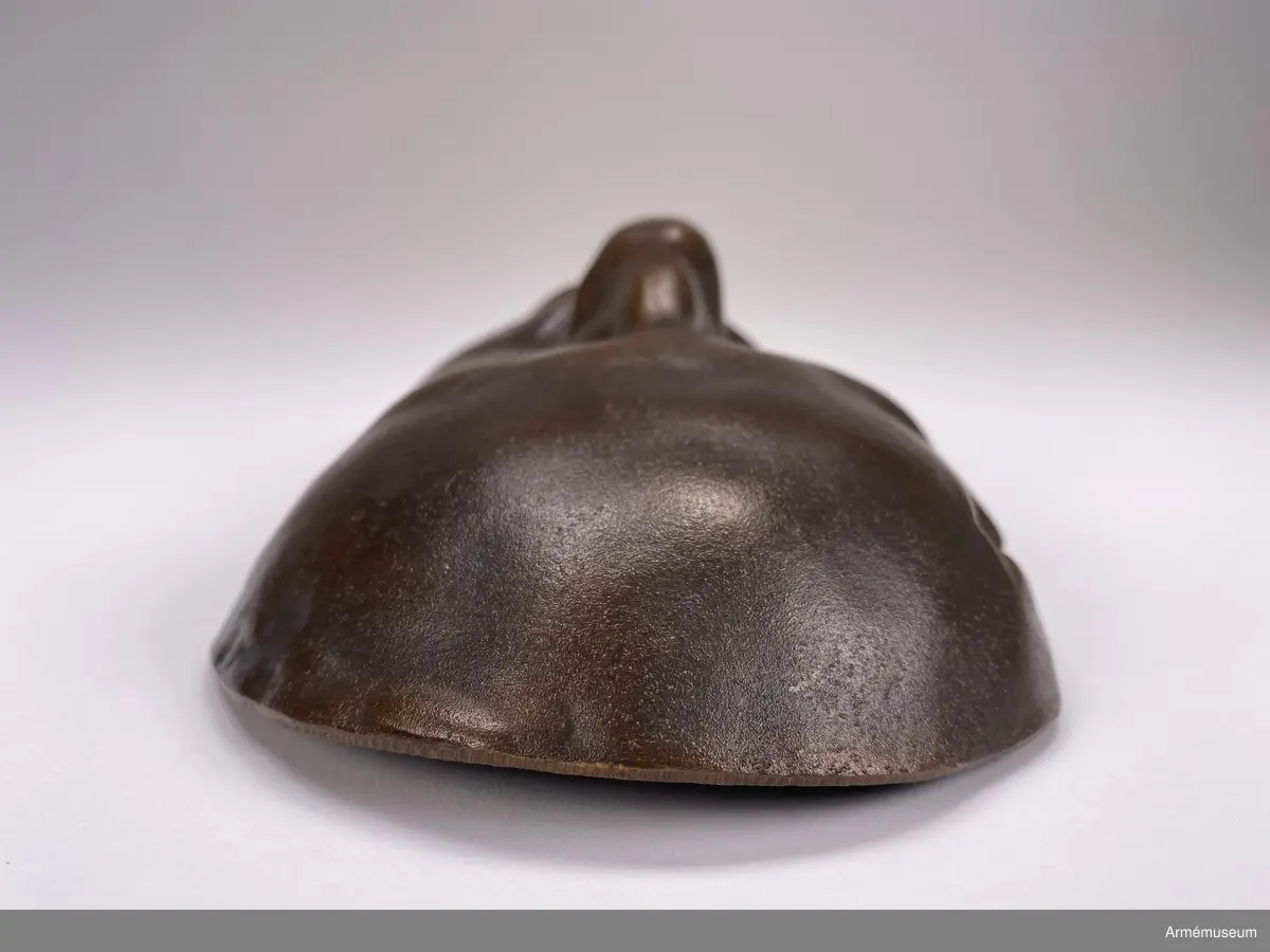 Bronsmask föreställande den döde Karl XII.

Enl styresman Olle Cederlöfs anteckningar med anledning av gåva AM.066063 (AM 73/475) är detta inte en dödsmask. 

"Proportionerna i ansiktet stämmer inte med kraniets proportioner enl 1918 års gravöppning - utan en av den schweiziske medaljgravören Hedlinger gjord frihandsmodellering inför konungens lik på Karlberg 1718. Hedlingers modell nu endast avsedd att ligga till grund för hans uppdrag: Att modellera en reliefbild för konungens mynt och minnespenningar. Hedlinger anlände till Sverige 1718-. Konungen hade då avlidit och Hedlinger hade aldrig sett Karl XII i levande livet, han tog chansen att fånga konungens ansikte inför 'lit de parade' på Karlberg. Hedlingers 'dödsmask' har senare avgjutits i gips, brons och  järn i olika sammanhang."