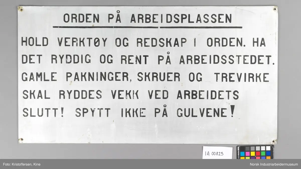 Metallskilt med informasjon om orden på arbeidsplassen. Ett hull i hvert hjørne, totalt fire hull.