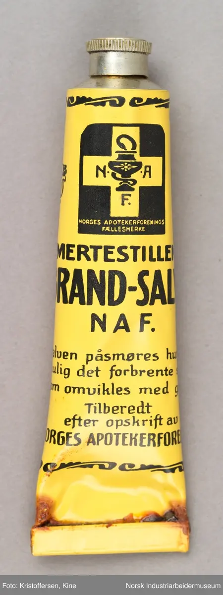 Tube med smertestillende brannsalve i original emballasje. Esken er avlang og gul med sort skrift-