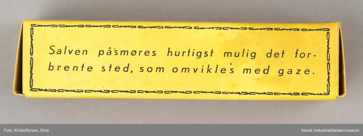 Tube med smertestillende brannsalve i original emballasje. Esken er avlang og gul med sort skrift-