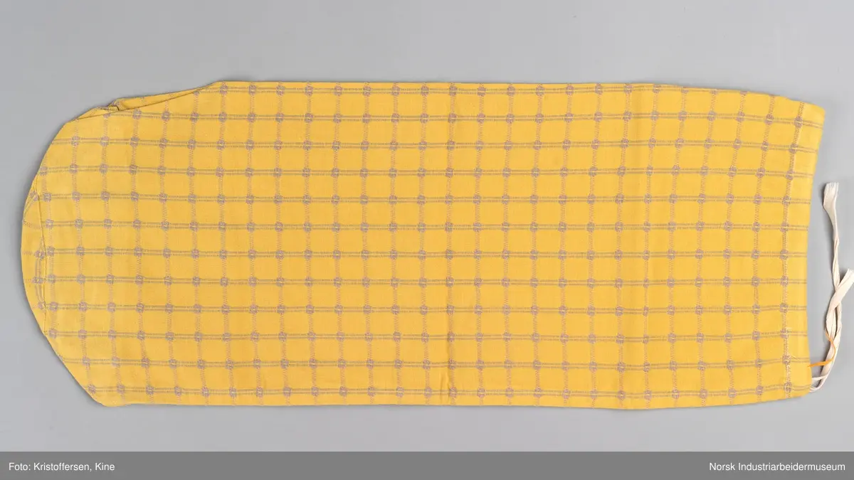 Tekstilpose. Det er søm i den ene siden av posen. Sømmen er en indresøm, det vil si ingen synlige falder og ikke noe stoff som kan trevles opp eller løse tråder på innsiden av posen. Bunnen er sydd av et rundt stoffstykke. Den er festet til posen med en vanlig søm, og kantene er kastet over for hånd. Det er løpegang oppe med bendelbånd gjennom. Dette kan ha vært et trekk til en pute, for eksempel en nakkepute, en pute som ligger i kortendene på en sofa eller seng som res opp om dagen. Det sitter en merkelapp på innsiden av sømmen i øverste kant. Det er en hvit lapp med rød skrift (maskinbroderi). Elektriker. Ovenfor dette merket er det sydd noen få, ujevne sting med beige brodergarn. Dette kunne ha vært en reparasjon, men det er ingen synlige skader i stoffet som skulle tilsi noe slikt. Det kan også være en vaskerimerking, eventuelt rester av en vaskerimerking. Det er også feste en liten, oransje tråd i kanten oppe. Det finnes noe liknende på andre av tekstilene – noe som kan tyde på at det er en merking som sier noe om avdelingen tekstilet hører til – eller det kan være en vaskerimerking. Det er søm i den ene siden av posen.