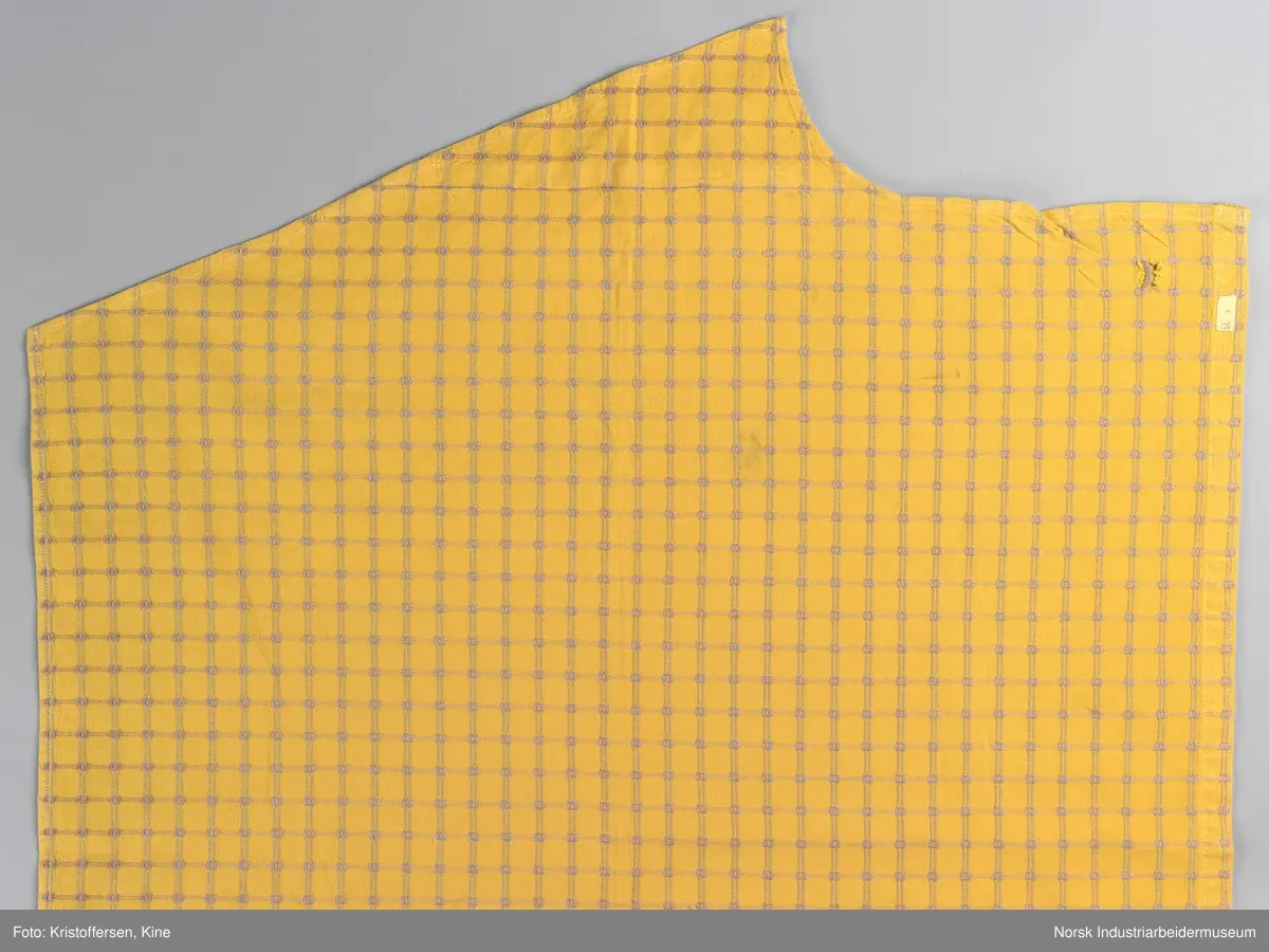 Gult stoffstykke satt sammen av tre stykker. Det er skjøtet 37 cm. fra høyre kant oppe. Pen skjøt, følger mønsteret. Jarekantene er ikke klippet av, men ligger på baksiden som sømningsmonn. På den andre siden, venstre side, er det satt på et lite stoffstykke ekstra. Det er gjort på samme måte, altså med en pen skjøt der mønsteret stemmer. Det er smale falder rundt hele stykket, men i overkant er den litt bredere. Det er et hull i stoffet. Stoffet er generelt ikke veldig slitt, og det virker ikke som dette hullet er forårsaket av alminnelig slitasje. Det må snarere være resultat av en spesiell påvirkning på akkurat det stedet. Pålimt lapp: F 09.