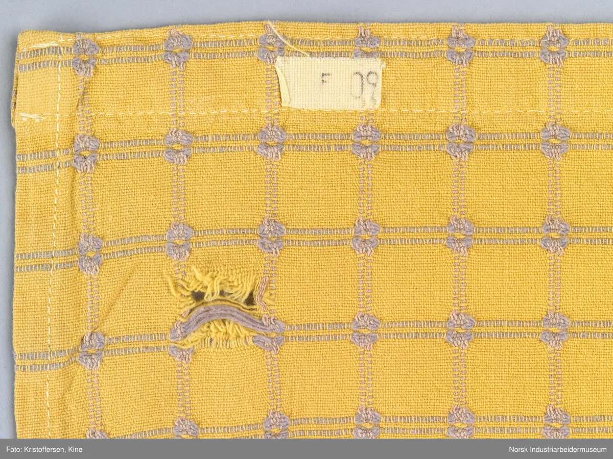Gult stoffstykke satt sammen av tre stykker. Det er skjøtet 37 cm. fra høyre kant oppe. Pen skjøt, følger mønsteret. Jarekantene er ikke klippet av, men ligger på baksiden som sømningsmonn. På den andre siden, venstre side, er det satt på et lite stoffstykke ekstra. Det er gjort på samme måte, altså med en pen skjøt der mønsteret stemmer. Det er smale falder rundt hele stykket, men i overkant er den litt bredere. Det er et hull i stoffet. Stoffet er generelt ikke veldig slitt, og det virker ikke som dette hullet er forårsaket av alminnelig slitasje. Det må snarere være resultat av en spesiell påvirkning på akkurat det stedet. Pålimt lapp: F 09.