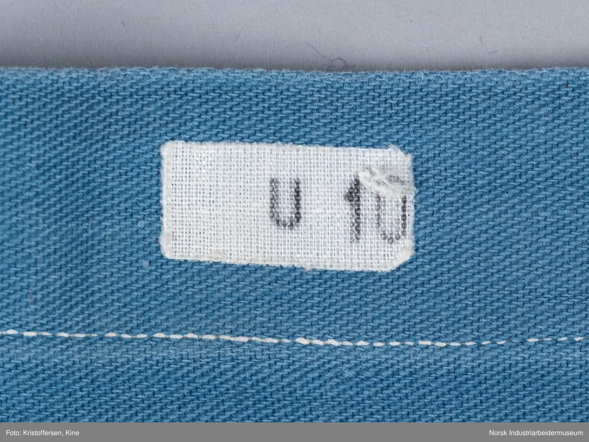 Putevaret er sydd sammen langs tre kanter og nederst er det en bredere fald der knytebåndene er festet. Det er to knytebånd på hver side, vanlige hvite bendelbånd. Pålimt merke: U 10. Det er også brodert en F i lysegrønn tråd ved sidesømmen i nedkant. Er begge deler vaskerimerking?
Det er ikke tvil om hva dette stoffstykket er – det er et putetrekk. Det er sydd av blått bomullsstoff, maskinvevd i kypertbinding. Putevaret er sydd sammen langs tre kanter og nederst er det en bredere fald der knytebåndene er festet. Det er to knytebånd på hver side, vanlige hvite bendelbånd. 
Pålimt merke: U 10. Det er også brodert en F i lysegrønn tråd ved sidesømmen i nedre kant. Er begge deler vaskerimerking? Eller er det merking som forteller hvor på båten putevaret hørte til?