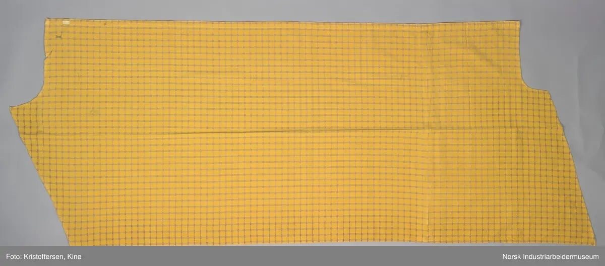 Gult stoffstykke satt sammen av tre stykker. Det er skjøtet 37 cm. fra høyre kant oppe. Pen skjøt, følger mønsteret. Jarekantene er ikke klippet av, men ligger på baksiden som sømningsmonn. På den andre siden, venstre side, er det satt på et lite stoffstykke ekstra. Det er gjort på samme måte, altså med en pen skjøt der mønsteret stemmer. Det er smale falder rundt hele stykket, men i overkant er den litt bredere. Det er et hull i stoffet. Stoffet er generelt ikke veldig slitt, og det virker ikke som dette hullet er forårsaket av alminnelig slitasje. Det må snarere være resultat av en spesiell påvirkning på akkurat det stedet. Pålimt lapp: F 09.