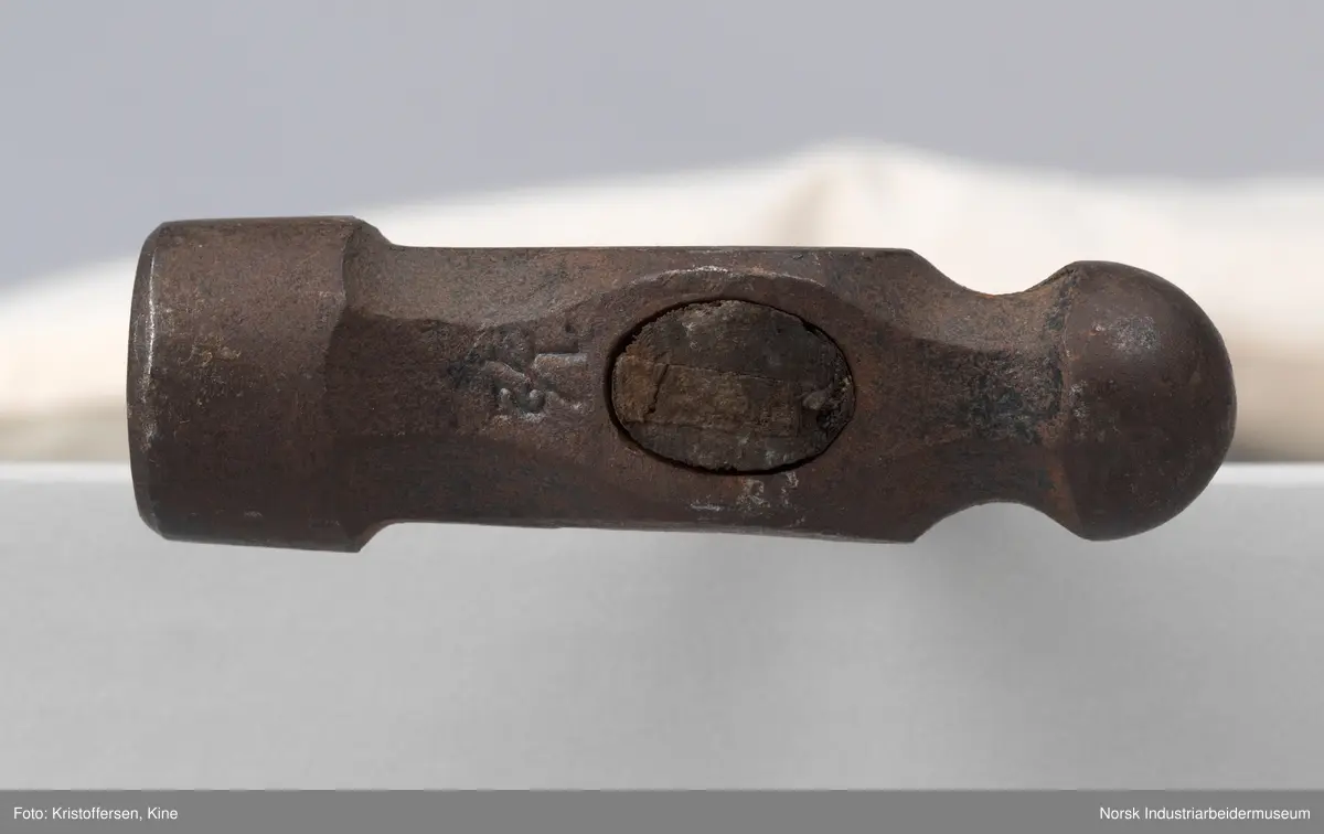Vognvisitørhammer. Skaftet er 79 cm. langt. Skaftet er gjennomgående. Hodet er veldig svart og sitter litt slarkete. Merking: Lok. 9 er svidd inn. På hammerhodet står det: ½ lbs. Germany. Det er også et stempel i form av en stigbøyle