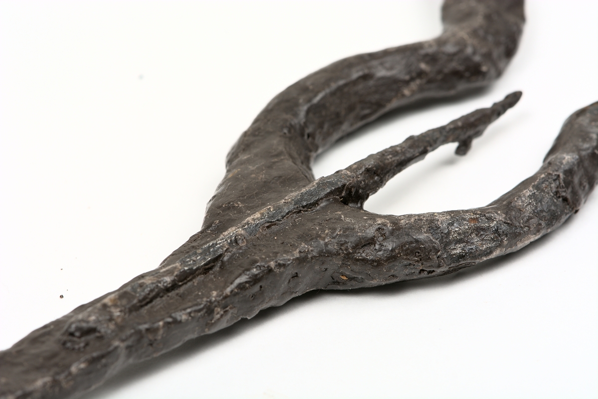 Ljuster av järn med spets inom starka, lyraformade sidostycken, som mitt för spetsen böjer av snett utåt sidorna.