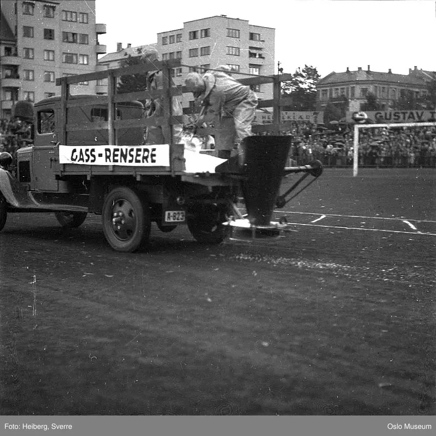 Frogner stadion, luftvern- og gassvernøvelse, mennesker, beskyttelsesdrakter, lastebil, tribuner, publikum, boligblokker, bygård