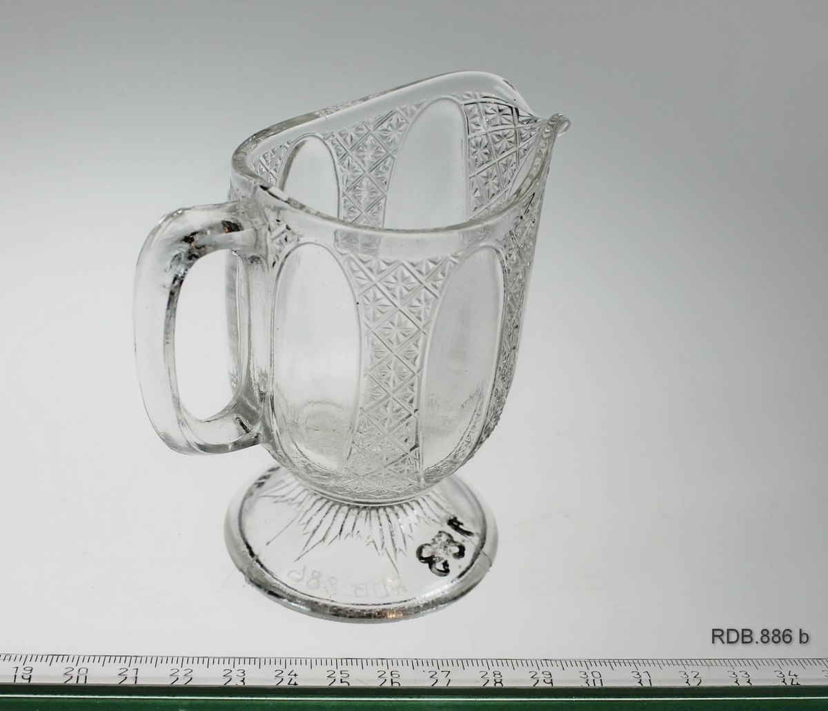 Fløtemugge i klart pressglass med stett og hank. Mugga er i god stand.