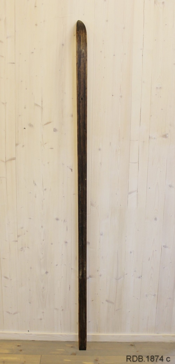 Avsmalende, jevnbred ski med liten bue. Bøy uten tupp. Rett avskåret bakende.
Dekorert med ei brun stripe på trehvit bunn.

Noen stempel fra OL øverst på skiet.
