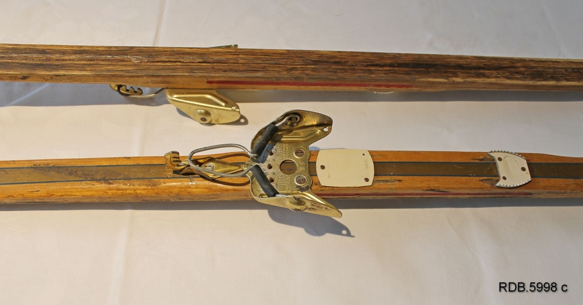 Et par laminerte treski. Trekvite med et bredt gullfarga felt kanta med en smal blå stripe langsetter skiet. Blå Splitkeinlogo på skituppen og blå påskrift. Påmontert gullfarga Rottefellabindinger. Bak disse er faststifta to kvite fotplater, den bakerste har metallkanter.