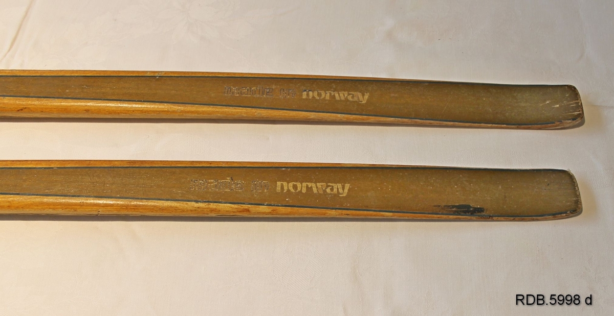 Et par laminerte treski. Trekvite med et bredt gullfarga felt kanta med en smal blå stripe langsetter skiet. Blå Splitkeinlogo på skituppen og blå påskrift. Påmontert gullfarga Rottefellabindinger. Bak disse er faststifta to kvite fotplater, den bakerste har metallkanter.