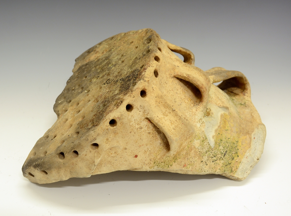 Fra protokollen: 
Keramikkskår. Tykt leirgods, flat bunn, utoverskrånende korpus som ender i en markert brutt kant oppe. Krukka har 4 dekorative ører nede på korpus og (1) og 2 større oppe. En mengde hull går inn i godset i bunnen og fra sidene av bunnen. Krukka mangler glasur, men har partivis (delvis) et slags grønnaktig belegg. Litt over halvparten av bunnen er bevart, men det meste av korpus er slått vekk. Krukka ble funnet i den under BM.1964:198, i merknadene, omtalte Bølebåten.