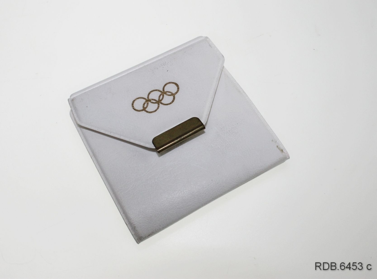 Gullfarget deltagerpin fra OL i Oslo 1952 til å feste på jakkeslaget. Selve pinen forestiller en fakkel med den olympiske ild med de olympiske ringer under. Under flammen står det 1952. Pinen er montert på en papplate med påskrift som ligger i en gjennomsiktig plastlomme. Plastlomma er festet til innsida av et kvitt plastetui som kan brettes sammen og lukkes med en trykknapp.
