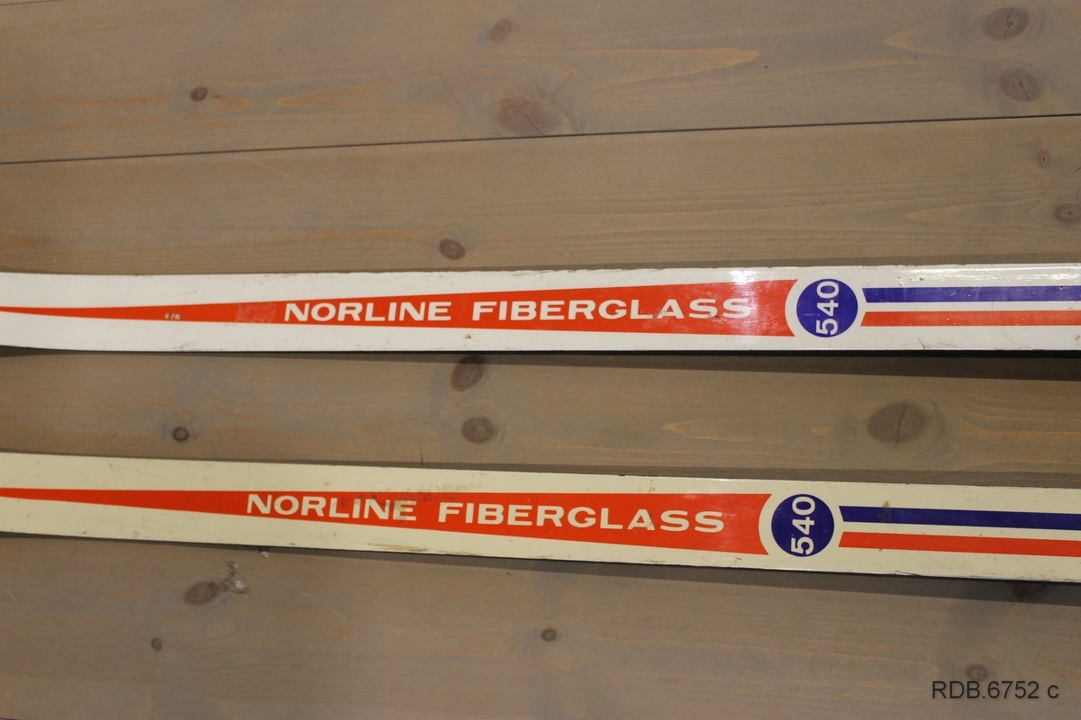 Et par Troll-ski, glassfiberski med trekjerne. Skiene er kvite med blå og røde dekorstriper og kvit påskrift. Skiene er jevnbrede men lett avfaset mot bakenden. Høg og spiss brett. Svarte sider og svart underside med ei egle. Påmontert blå Rottefellabindinger og kvit hælstøtte.