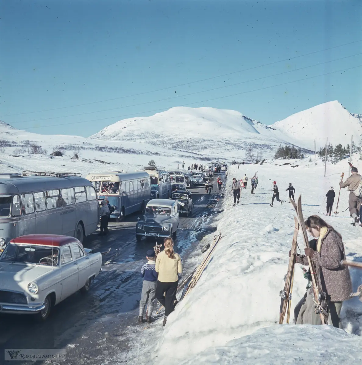 Ørskogfjellet..Mange fra Ålesundområdet reiste dit når det var gode forhold for skitur. Bussene er sannsynligvis fra 1950-tallet og det er få personbiler å se. Folk var mer avhengig av buss den gangen. Den fremste bussen, grålakkert, tilhørte Vestnesruten, som hadde ruter Ålesund-Vestnes i korrespondanse med fergene til og fra Molde. De neste to bussene tilhørte Skodjeruta som hadde busser lakkert i blått og gult. Den første av disse to minner om T-1042, 1955-modell, som er bevart og eksisterer som veteranbuss..Nærmeste bil: Ford Consul 1956-ca. 61, fulgt av Volvo Duett.