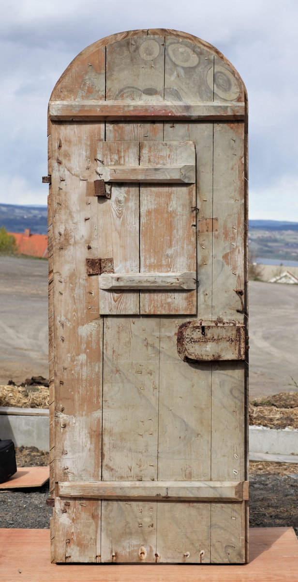 Døra er laget av 1 1/4 toms planker med to enkle drev som holder plankene sammen. Døra er belagt med profilert panel. Panelet er lagt på skrå i mønemønster og festet med spiker som har digre hoder. Døra har et vindu på 45 cm x 79 cm som innvendig er lukket med en liten hengslet dør. Døra er nærmest halvsirkelformet i toppen og passer da inn i buen i murverket. Låsen sitter på og har rombeformet nøkkelhullbeslag og to solide gangjern med to enkle knuter. Låsen sitter på innsida og er helt innebygd med jernplater og to slåtter. På innsida er rester etter påmalt marmorering.