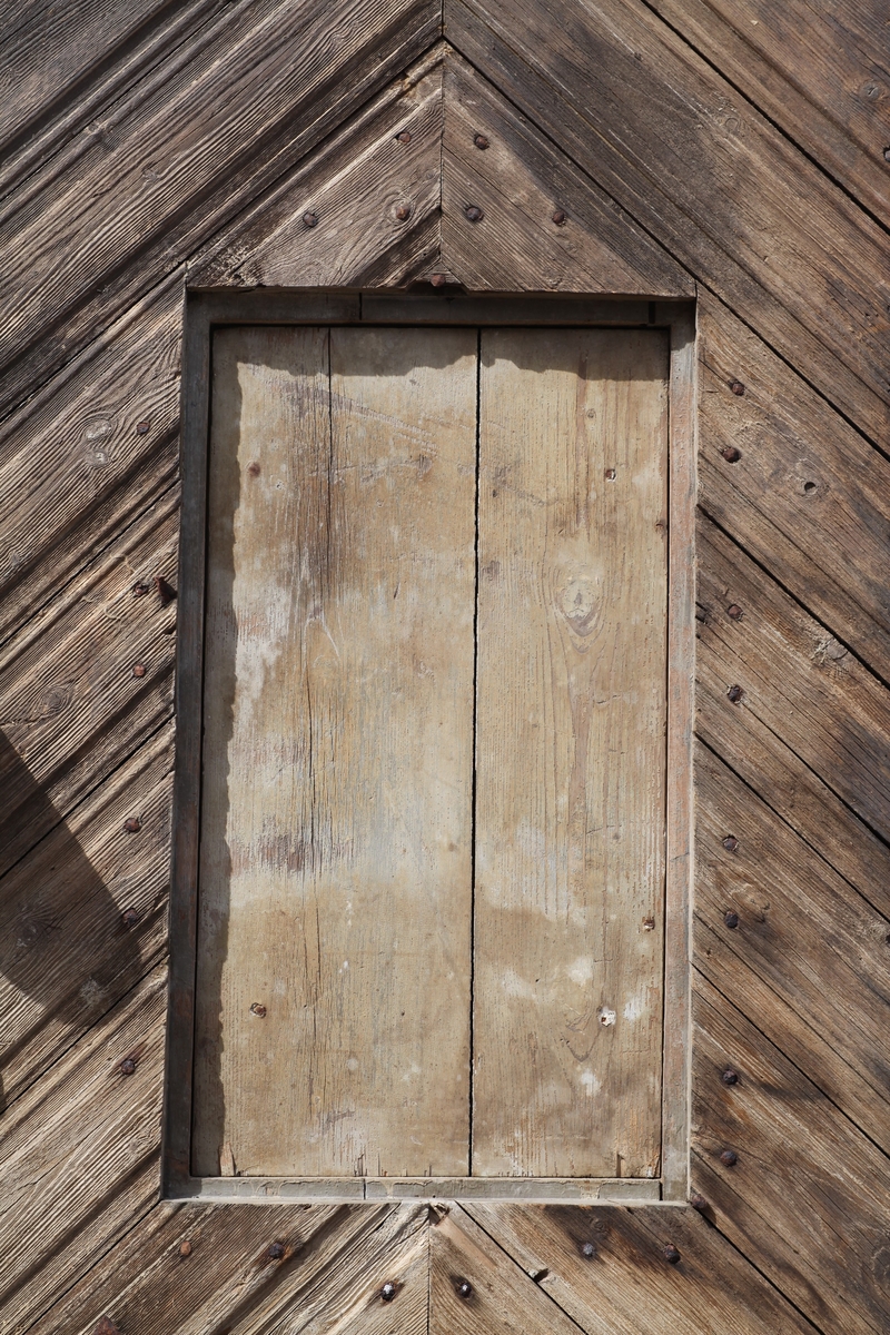 Døra er laget av 1 1/4 toms planker med to enkle drev som holder plankene sammen. Døra er belagt med profilert panel. Panelet er lagt på skrå i mønemønster og festet med spiker som har digre hoder. Døra har et vindu på 45 cm x 79 cm som innvendig er lukket med en liten hengslet dør. Døra er nærmest halvsirkelformet i toppen og passer da inn i buen i murverket. Låsen sitter på og har rombeformet nøkkelhullbeslag og to solide gangjern med to enkle knuter. Låsen sitter på innsida og er helt innebygd med jernplater og to slåtter. På innsida er rester etter påmalt marmorering.