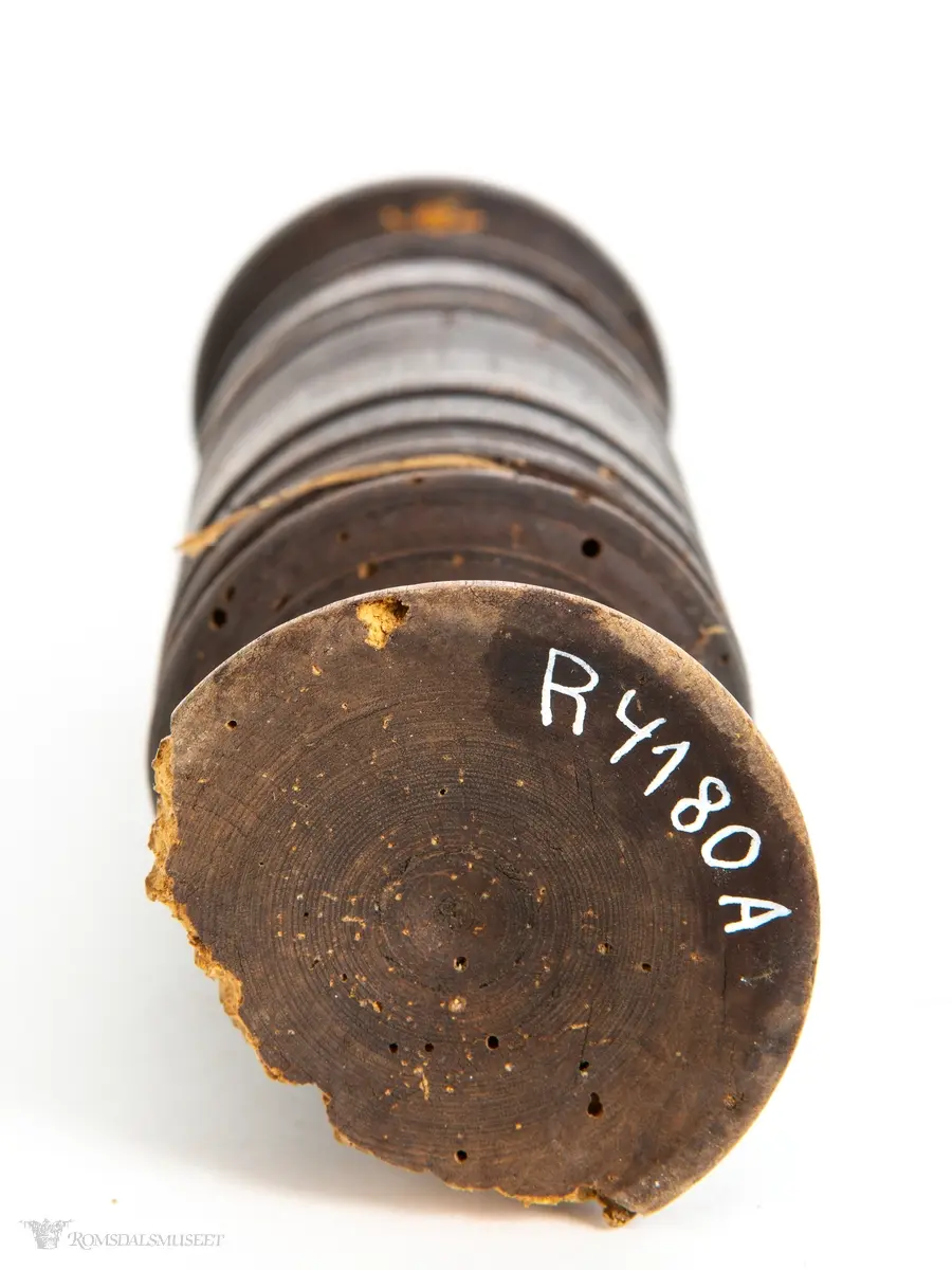 Dreid hylse med liten stett, og pistill med rundt, flatt håndgrep. Jernplate spikret fast i enden av pistillen.