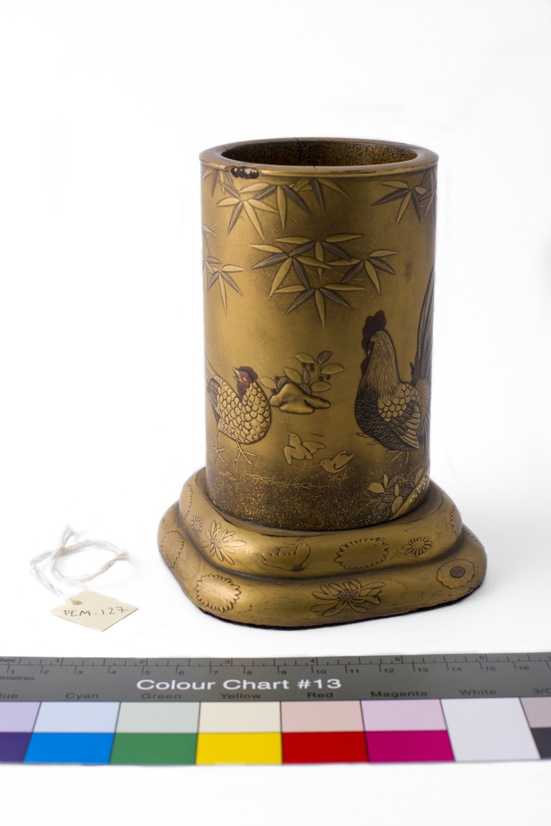 Rund vase av bambus (?) på avrundet, firkantet sokkel. Malt, lakkert eller glasert i relieff med motiv av bambus, blomster, hane, høne, orientalsk landskap.