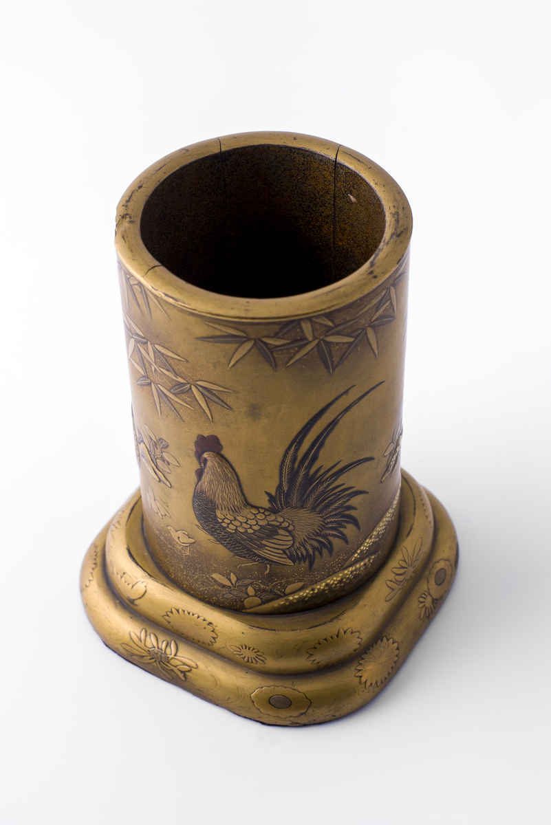 Rund vase av bambus (?) på avrundet, firkantet sokkel. Malt, lakkert eller glasert i relieff med motiv av bambus, blomster, hane, høne, orientalsk landskap.