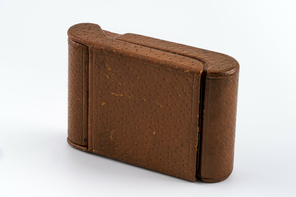 Reiseklokke fra merket Angelus fra Sveits. Ur med i messingfarge festet i brunt skinnetui. Med lokk som i åpen posisjon fungerer som støtte slik at det kan stå på bordet. Uret kan vippes fram for å avdekke baklokk med innstillingsknapper. Har tilhørt Sara Fabricius.