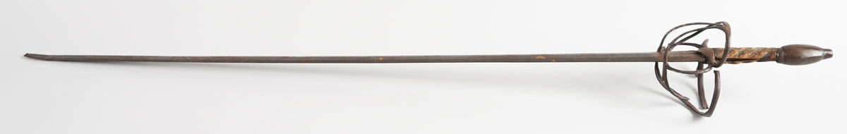 Kårde. Lang, rett klinge med tre kantar (på kvar side). Handtak i tre med spiralliner, solid jarnknapp nedst og metall handbeskyttelse. På kva side av klinga, ned mot handtaket, er det gravert tre kross eller stjerner, og innimellom første og andre stjerne, eit løpande dyr.