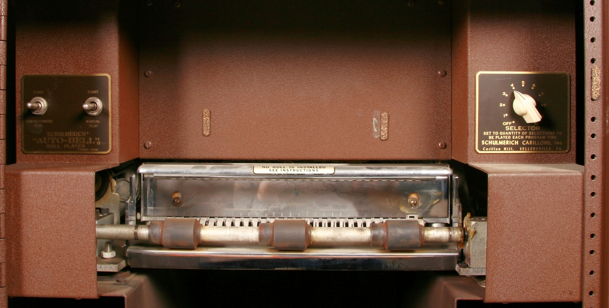 To brunmalte skap i metall (samme størrelse). Flere ventilasjonsrister.

Det ene skapet (A) inneholder avspiller, forsterker, klokkemekanikk, liten høytaler og øvrig elektronikk (noen deler ser ut å mangle). 
Øvre halvdel: bak pleksiglass som kan lukkes er styresentralen med instillinger for ulike klokkeprogrammer:
Til høyre er switch-knapper for å aktivere de tre funksjonene 
a) avspilling av musikkrull 
b) bruk av manuelt spillebord og 
c) timeslag.

Over til venstre er en timer for å skjemalegge de ulike aktivitetene:
1) Hverdag avspilling musikkrull
2) Søndag avspilling musikkrull
3) Hverdag avspilling timeslag
4) Søndag avspilling timeslag
5) Hverdag avspilling manuelt spillebord
6) Søndag avspilling manuelt spillebord

I tillegg er et eget panel for å velge ulike fomer av klokkeringinger ('BELL PEAL').

Nedre halvdel: Musikkrullmekanikk med en mekanisk avleser for musikkrullene ('tracker bar'). 30 spor; én for én tone hver. Papirullen løper over en rekke fjærbelastede(?) L-formet tangenter, en for hvert spor. Når et hull passerer en tangent løftes tangenten oppover og gir i sin tur et signal videre om å aktivere akkurat denne tonen.

Det andre skapet (B) idag tomt, usikker funksjon. Har strømforsyning. Sannsynlig forsterker for bruk av høytalere (C-F) i klokketårnet. Se elektronikk (H). Muligens også oppbevaring av musikkruller med mer.