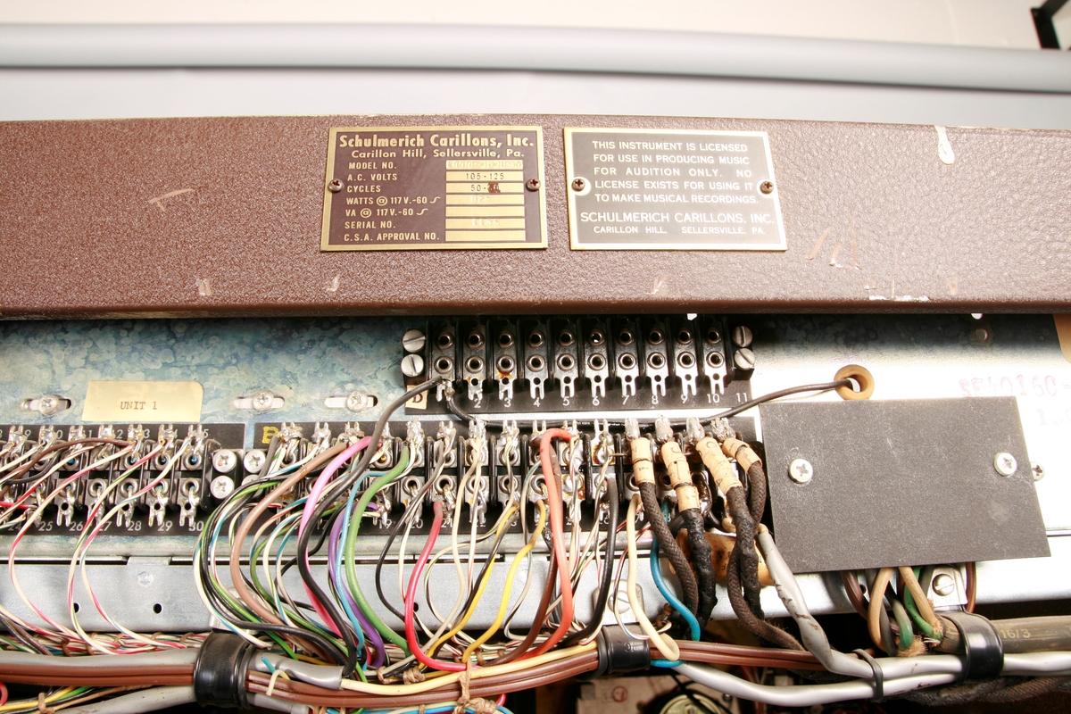 To brunmalte skap i metall (samme størrelse). Flere ventilasjonsrister.

Det ene skapet (A) inneholder avspiller, forsterker, klokkemekanikk, liten høytaler og øvrig elektronikk (noen deler ser ut å mangle). 
Øvre halvdel: bak pleksiglass som kan lukkes er styresentralen med instillinger for ulike klokkeprogrammer:
Til høyre er switch-knapper for å aktivere de tre funksjonene 
a) avspilling av musikkrull 
b) bruk av manuelt spillebord og 
c) timeslag.

Over til venstre er en timer for å skjemalegge de ulike aktivitetene:
1) Hverdag avspilling musikkrull
2) Søndag avspilling musikkrull
3) Hverdag avspilling timeslag
4) Søndag avspilling timeslag
5) Hverdag avspilling manuelt spillebord
6) Søndag avspilling manuelt spillebord

I tillegg er et eget panel for å velge ulike fomer av klokkeringinger ('BELL PEAL').

Nedre halvdel: Musikkrullmekanikk med en mekanisk avleser for musikkrullene ('tracker bar'). 30 spor; én for én tone hver. Papirullen løper over en rekke fjærbelastede(?) L-formet tangenter, en for hvert spor. Når et hull passerer en tangent løftes tangenten oppover og gir i sin tur et signal videre om å aktivere akkurat denne tonen.

Det andre skapet (B) idag tomt, usikker funksjon. Har strømforsyning. Sannsynlig forsterker for bruk av høytalere (C-F) i klokketårnet. Se elektronikk (H). Muligens også oppbevaring av musikkruller med mer.