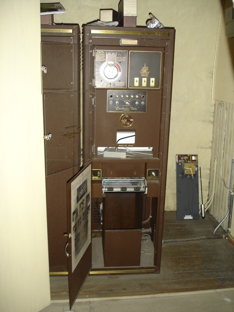 To brunmalte skap i metall (samme størrelse). Flere ventilasjonsrister.

Det ene skapet (A) inneholder avspiller, forsterker, klokkemekanikk, liten høytaler og øvrig elektronikk (noen deler ser ut å mangle). 
Øvre halvdel: bak pleksiglass som kan lukkes er styresentralen med instillinger for ulike klokkeprogrammer:
Til høyre er switch-knapper for å aktivere de tre funksjonene 
a) avspilling av musikkrull 
b) bruk av manuelt spillebord og 
c) timeslag.

Over til venstre er en timer for å skjemalegge de ulike aktivitetene:
1) Hverdag avspilling musikkrull
2) Søndag avspilling musikkrull
3) Hverdag avspilling timeslag
4) Søndag avspilling timeslag
5) Hverdag avspilling manuelt spillebord
6) Søndag avspilling manuelt spillebord

I tillegg er et eget panel for å velge ulike fomer av klokkeringinger ('BELL PEAL').

Nedre halvdel: Musikkrullmekanikk med en mekanisk avleser for musikkrullene ('tracker bar'). 30 spor; én for én tone hver. Papirullen løper over en rekke fjærbelastede(?) L-formet tangenter, en for hvert spor. Når et hull passerer en tangent løftes tangenten oppover og gir i sin tur et signal videre om å aktivere akkurat denne tonen.

Det andre skapet (B) idag tomt, usikker funksjon. Har strømforsyning. Sannsynlig forsterker for bruk av høytalere (C-F) i klokketårnet. Se elektronikk (H). Muligens også oppbevaring av musikkruller med mer.