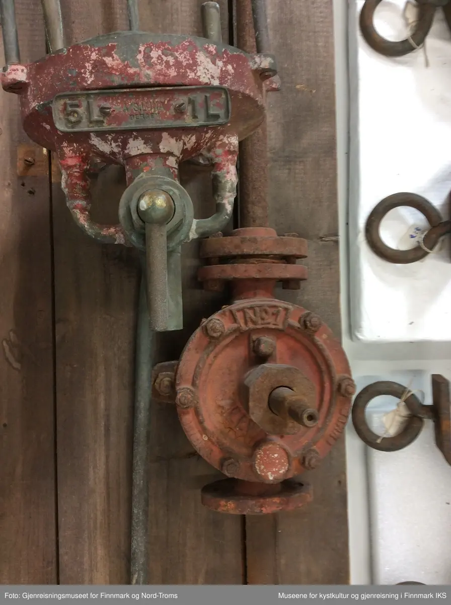 Bensinpumpa består av metall og har forskjellige ventiler. Den er festet til ei bakplate bestående av 3 planker som er avrundet oppe. På baksida er platen stabilisert med tverrgående bord oppe, nede og i midten. Pumpens glassbeholder er knust og fjernet. 